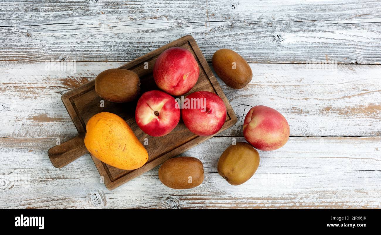 White rustic table with assorted fruit consisting of peach, kiwi, and mango in overhead view layout Stock Photo