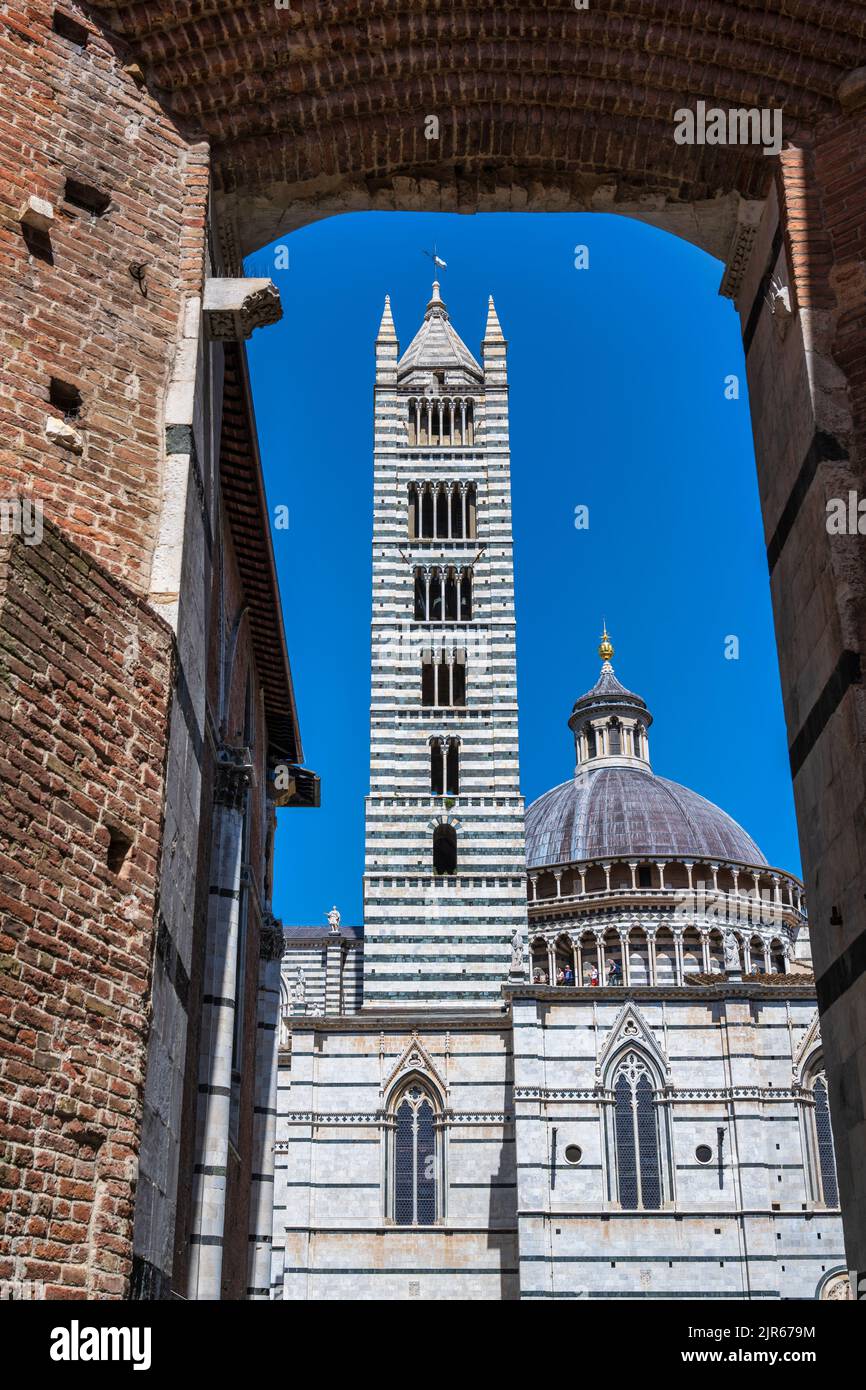 View of the Campanile (bell tower) and Dome of Siena Duomo (Siena Cathedral) through arch in Via del Castoro in Siena, Tuscany, Italy Stock Photo