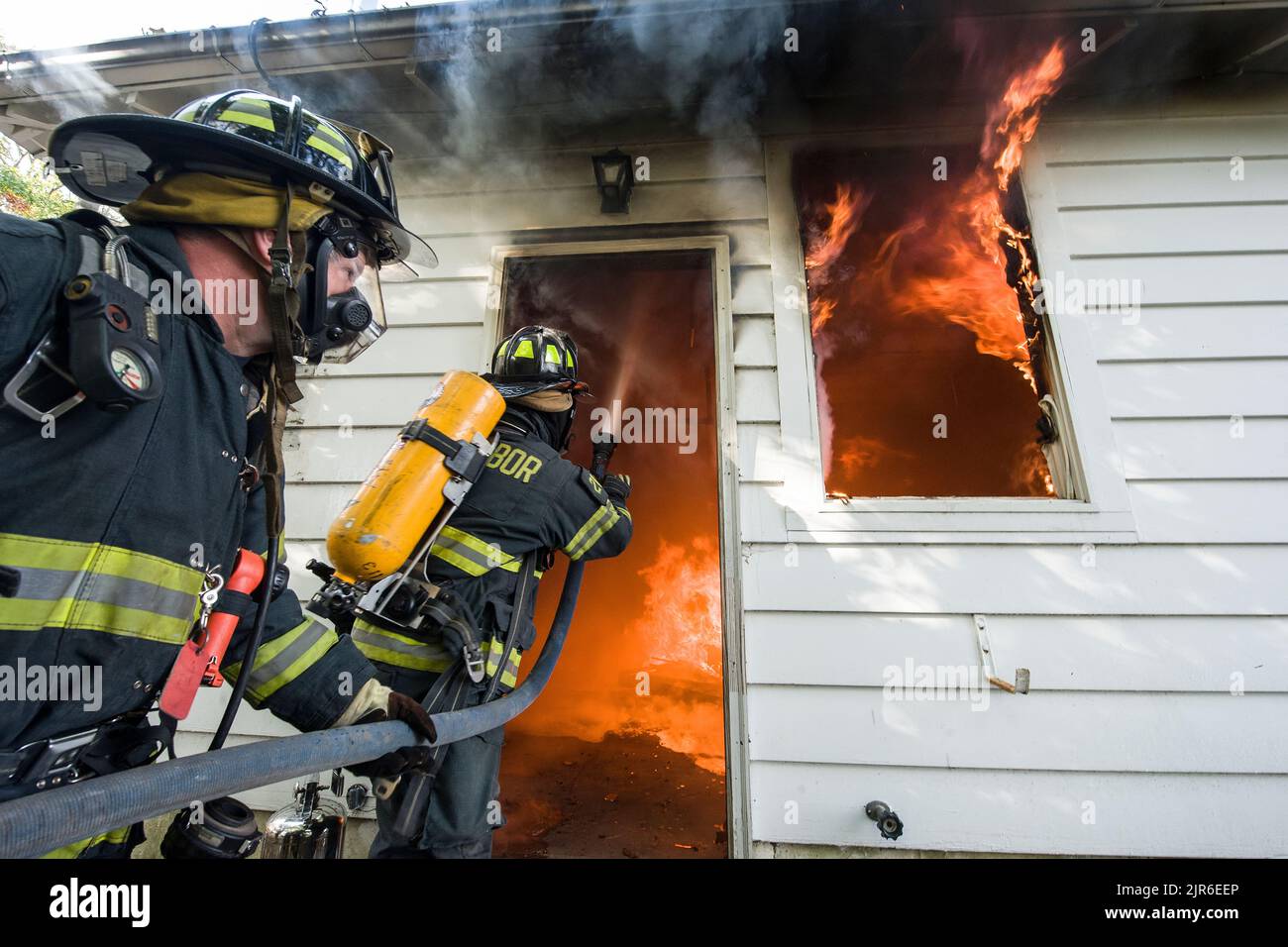 A Sag Harbor firefighter trains a hose stream through a doorway onto the ceiling as firefighters from the Sag Harbor Fire Department were joined by me Stock Photo
