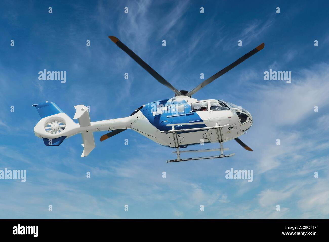 Blue and white air ambulance rescue helicopter flying mid-air against a blue sky background Stock Photo
