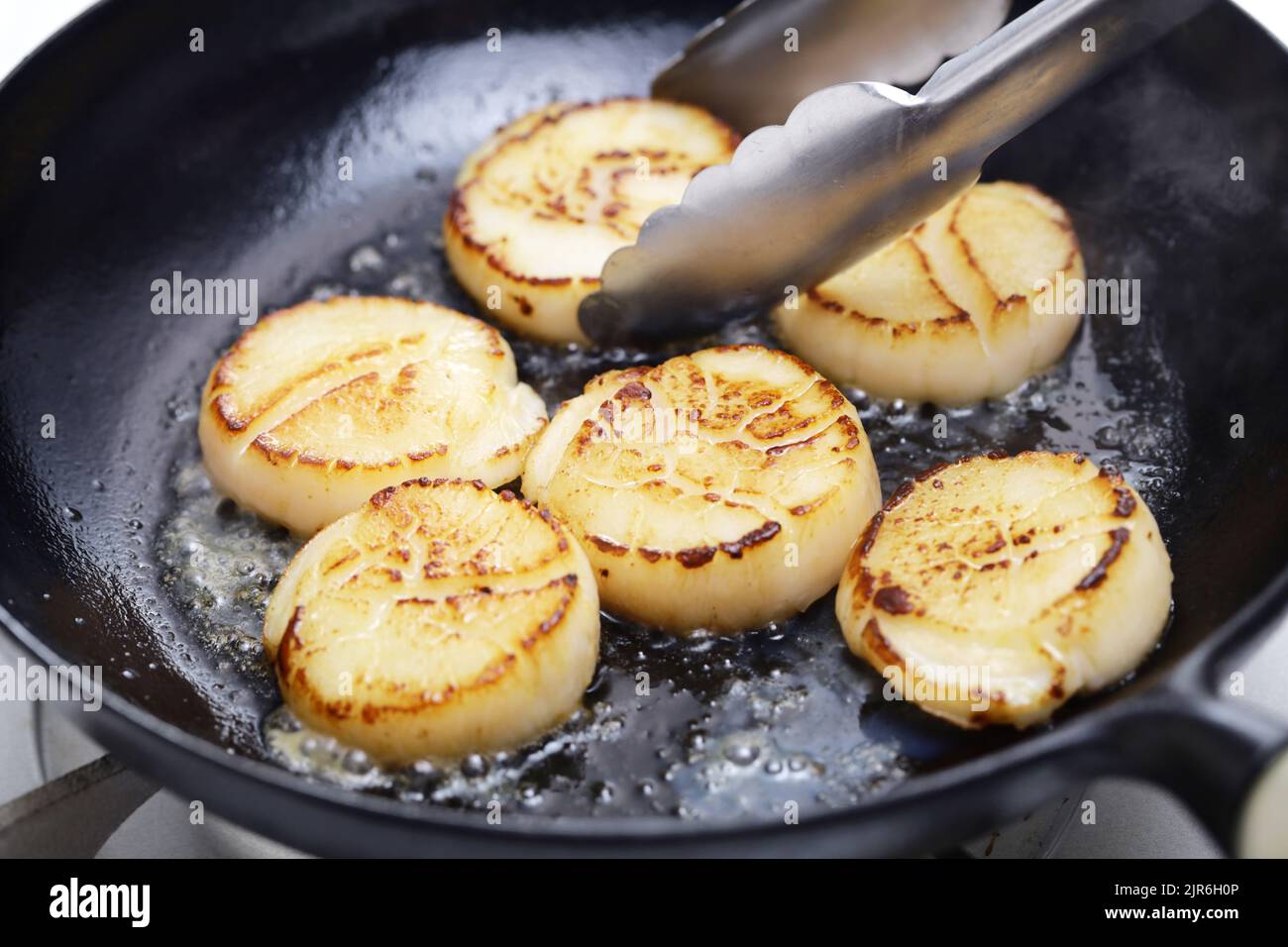 seared scallops in cast iron pan with tongs Stock Photo