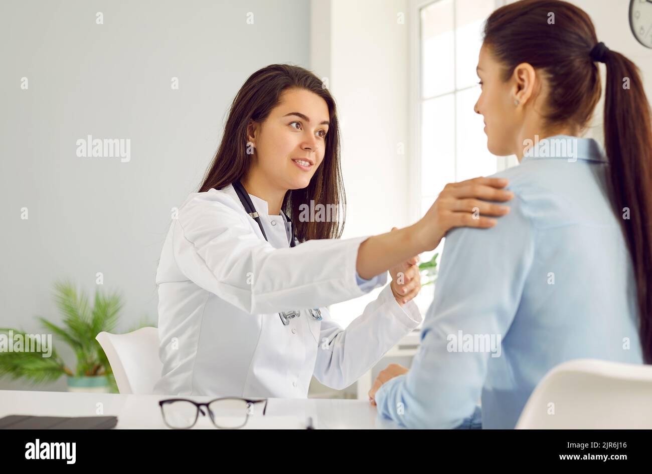 Supportive doctor reassuring young woman during medical consultation at ...