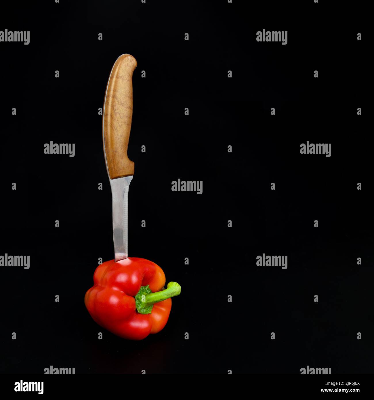 A sharp knife is stuck in Red pepper on black background Stock Photo