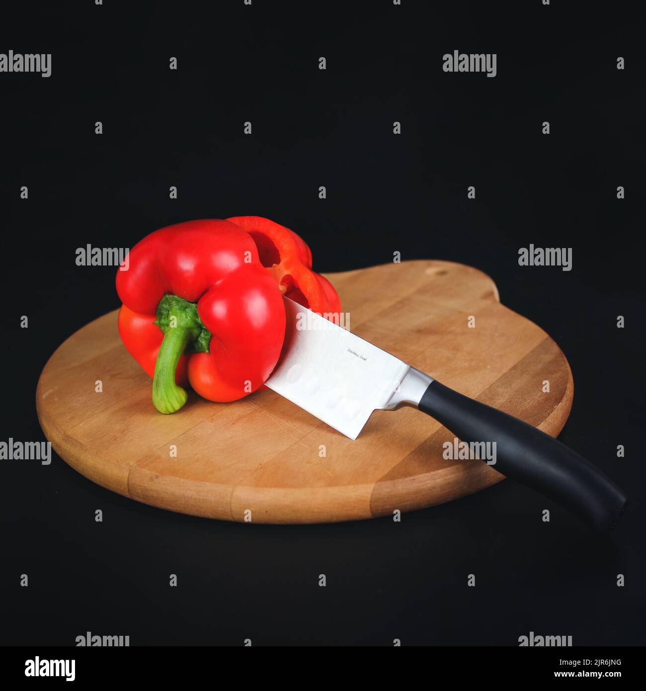 Big kitchen knife cut a bell pepper on two parts close up on wooden board. Stock Photo