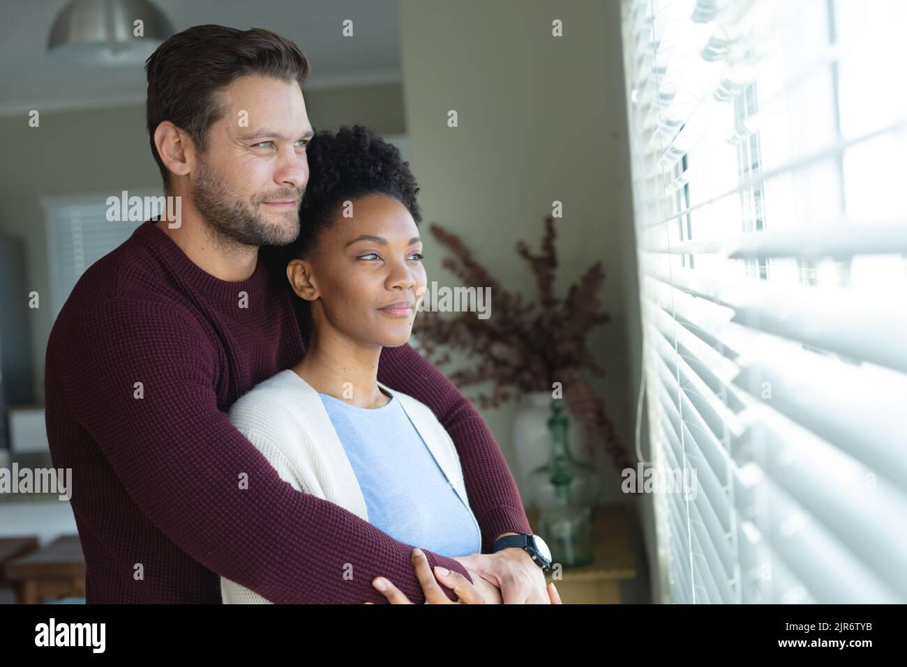 Image of diverse couple embracing and looking outside window Stock ...