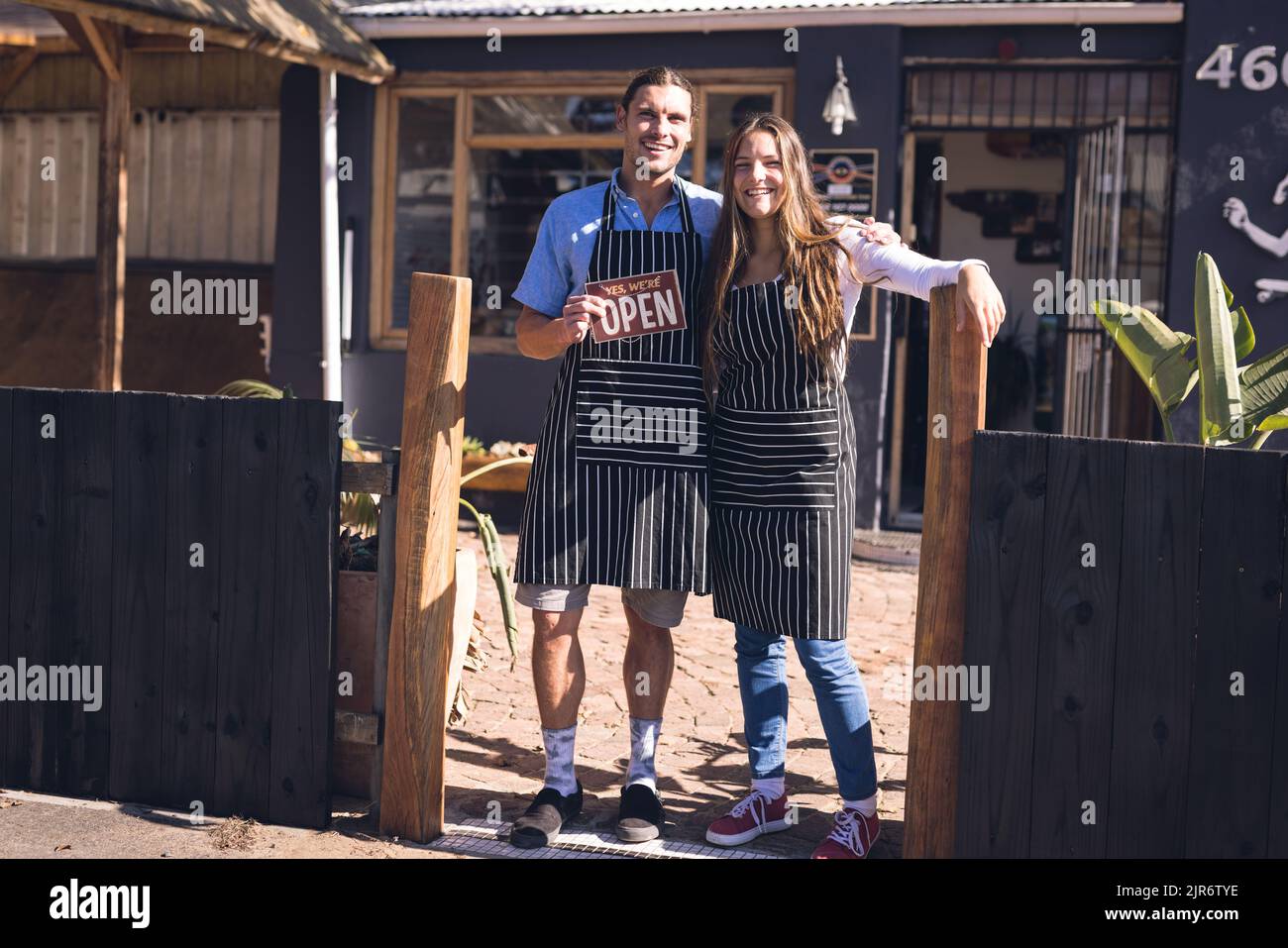 Image of happy caucasian woman and man in aprons and open sign in front of skate shop Stock Photo