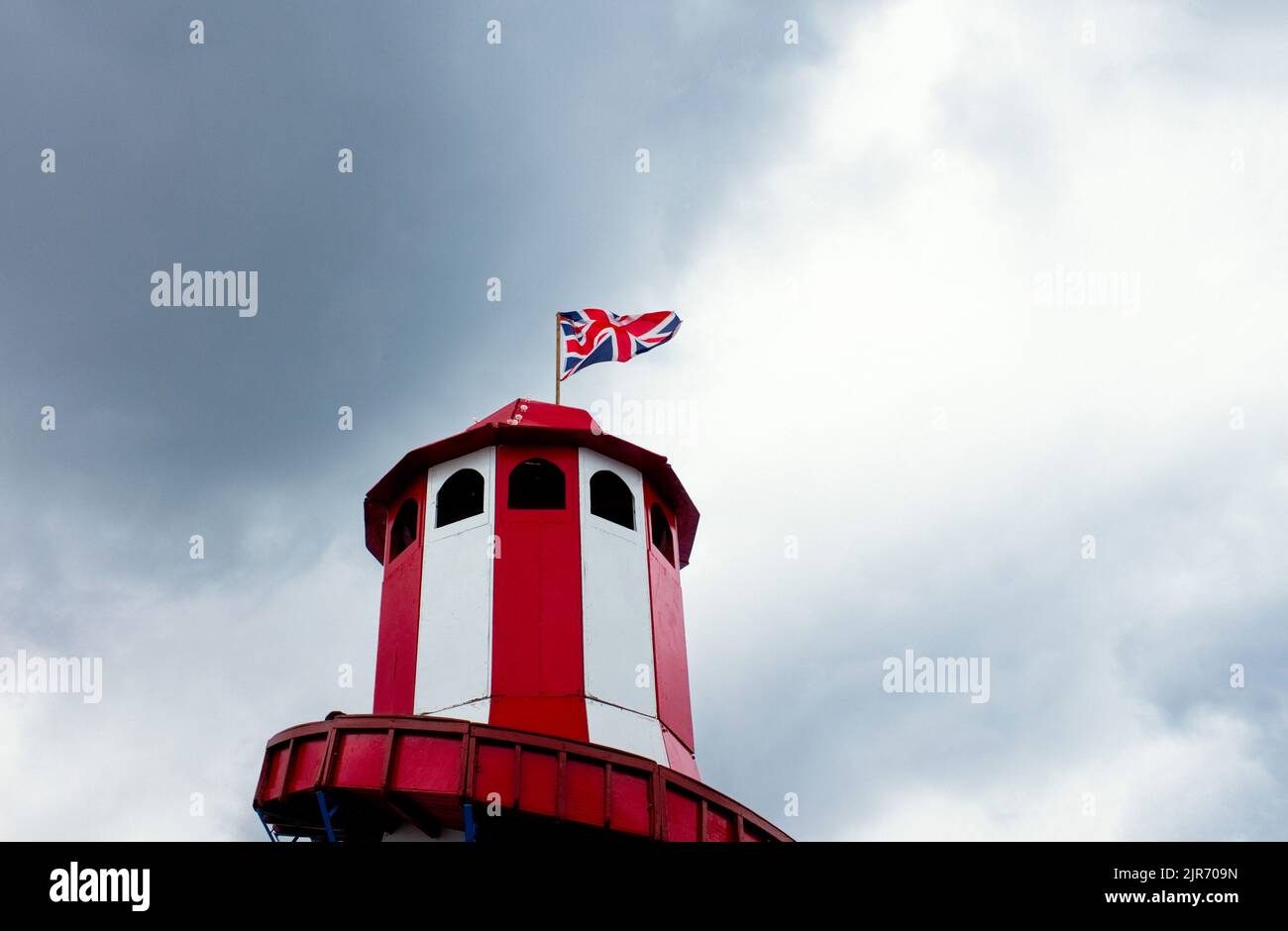 Looking up at a helter skelter with a union jack flag flying at the top against a dark cloudy sky Stock Photo