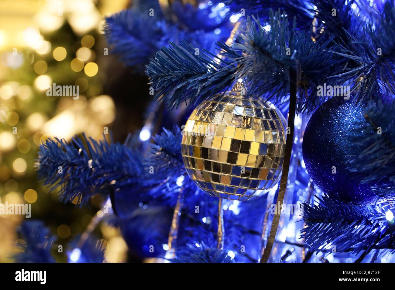 Christmas tree with blue and mirror balls in a shopping mall on background of blurred festive lights. New Year toys and decorations, winter holidays Stock Photo