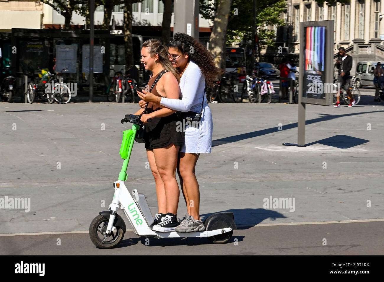Antwerp, Belgium - August 2022: Two people balancing on an electric scooter in the city centre. One is using a mobile phone while holding on Stock Photo
