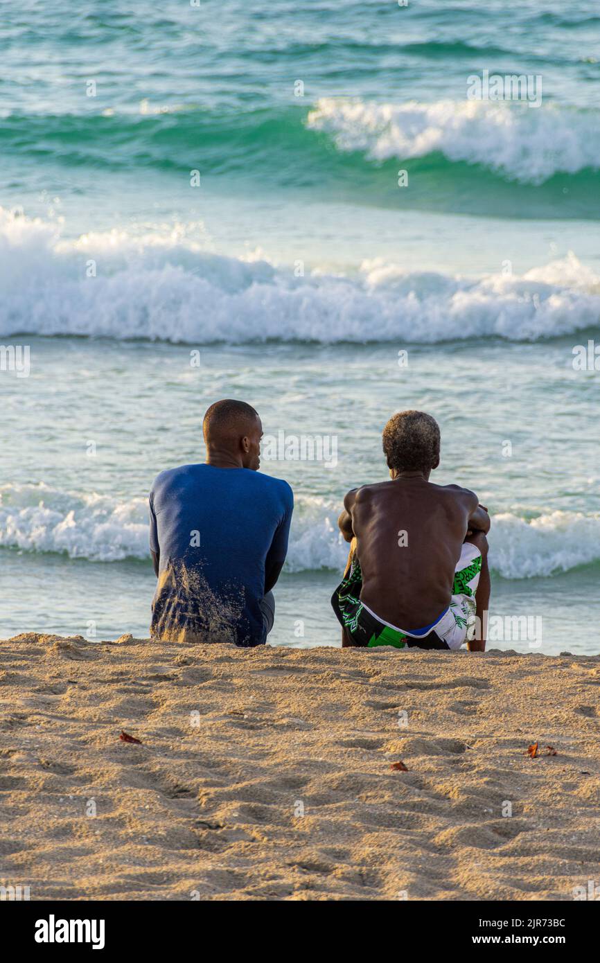 Two Cuban, men sitting on the beach talking, Varadero Beach, Cuba. Stock Photo