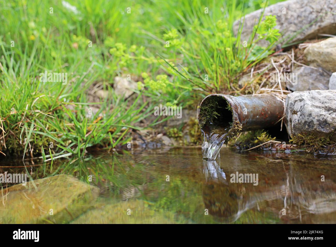 crystal clear water pouring from a metal pipe in the mountains Stock Photo