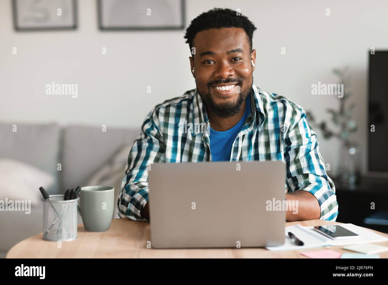 Cheerful Black Man At Laptop Computer Wearing Earbuds Working Indoors Stock Photo