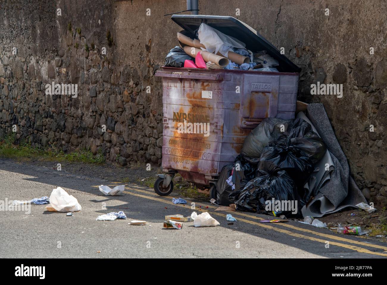 overflowing wheelie bin at the side of a street with litter falling