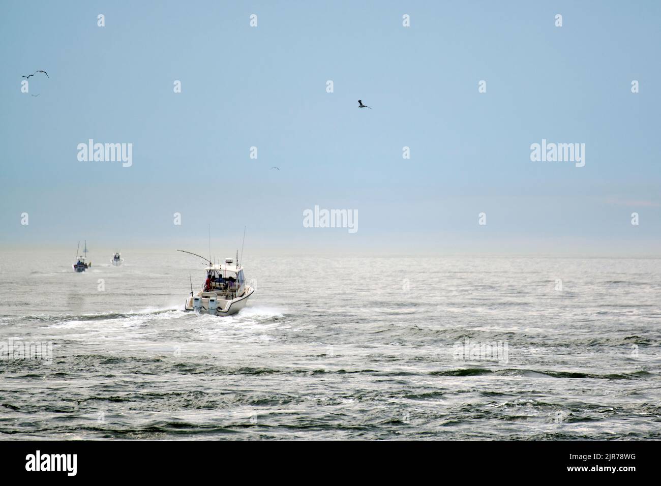 Sport fishing boats head to sea on a misty summer morning from Indian River Inlet in Sussex County, Delaware USA. Stock Photo