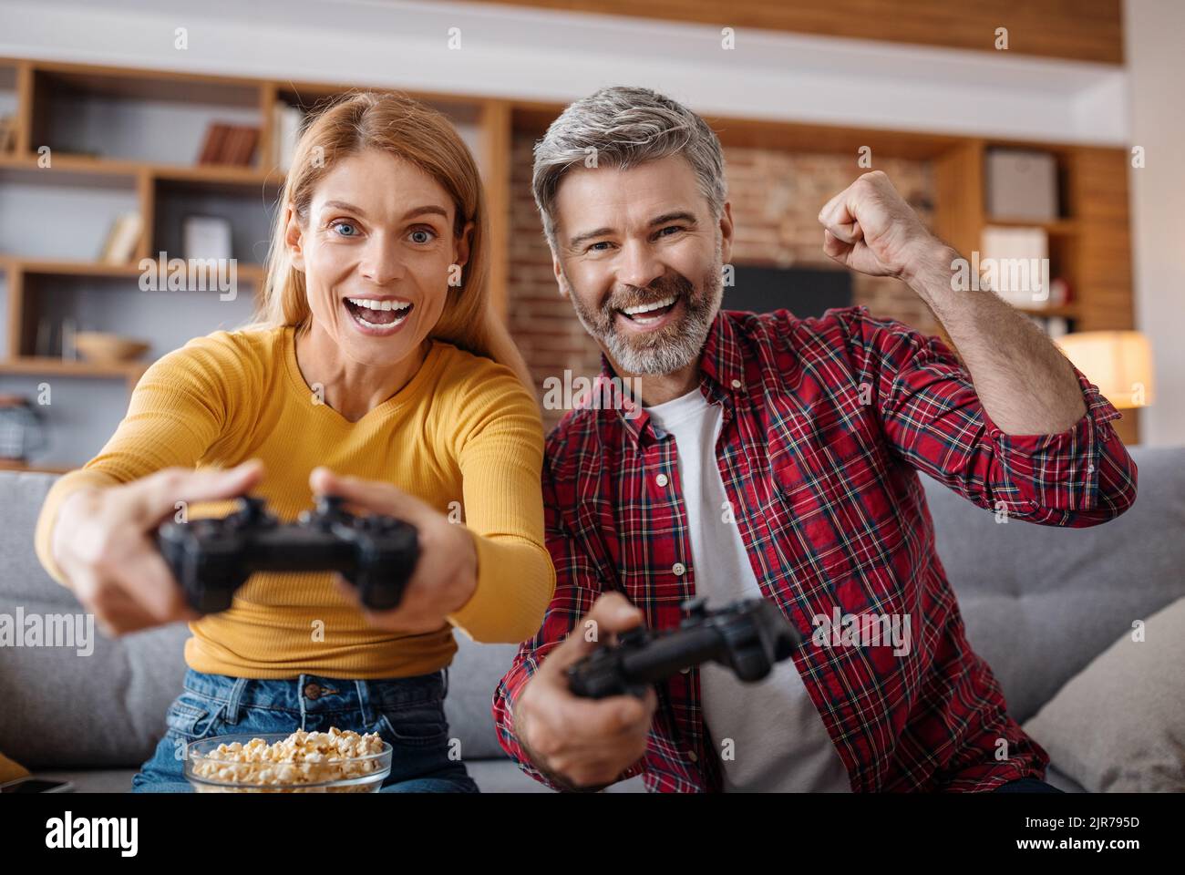 Glad excited adult caucasian female and male with joysticks play in online game in free time, celebrate victory Stock Photo