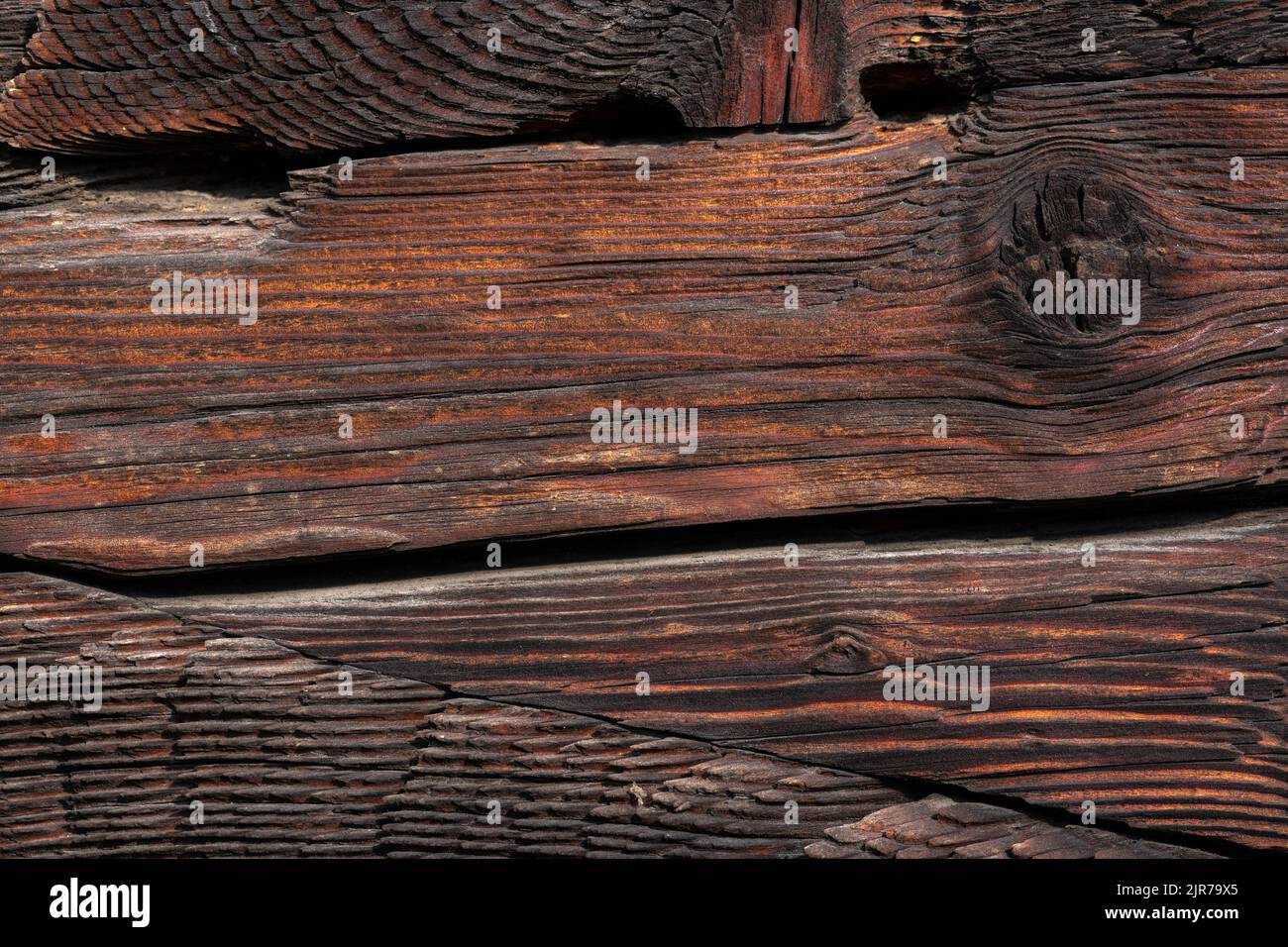 Macro shot of an ancient weathered dark brown cracked wood beam surface with nice rough grain texture. Stock Photo