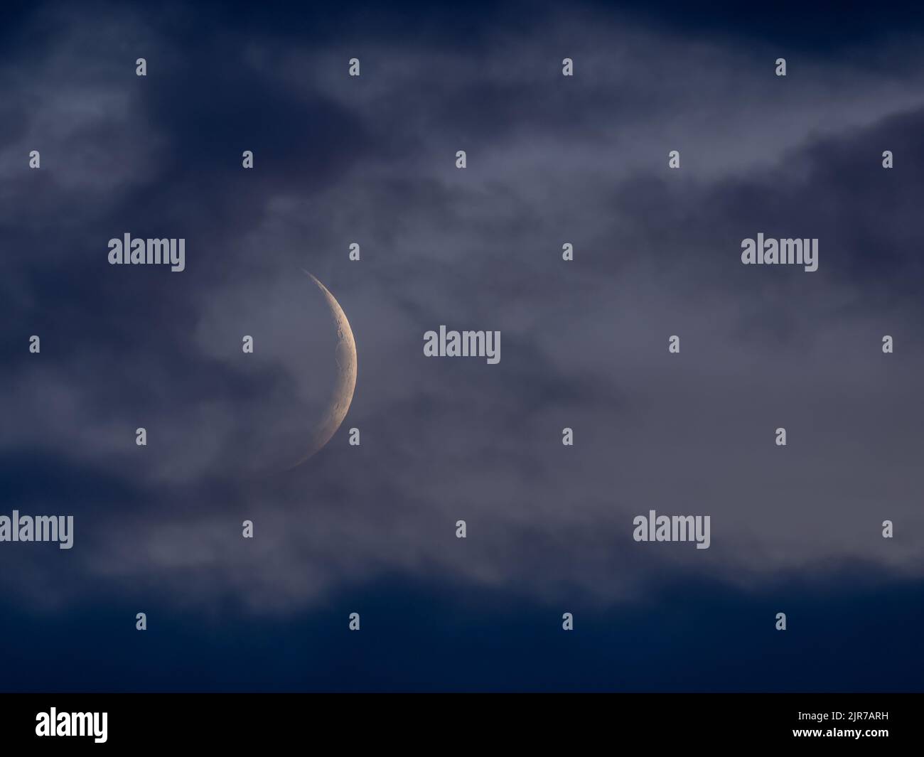 Waxing crescent Moon through light grey cloud Stock Photo