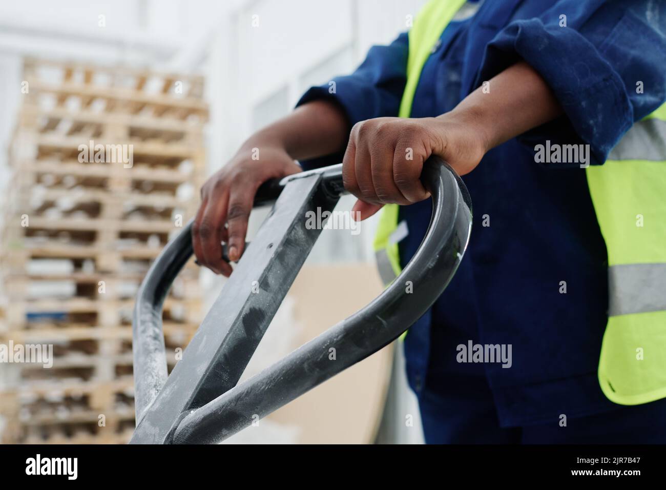 Hands of young black woman in uniform holding by handle of forklift loader with pallets while pushing it forwards during work Stock Photo