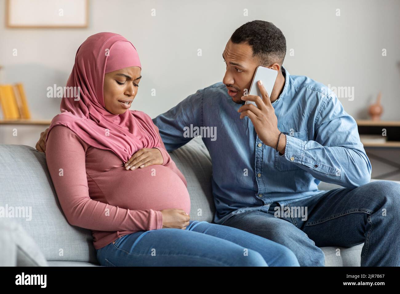 Worried Man Calling Doctor While His Pregnant Muslim Wife Suffering Prenatal Contractions Stock Photo