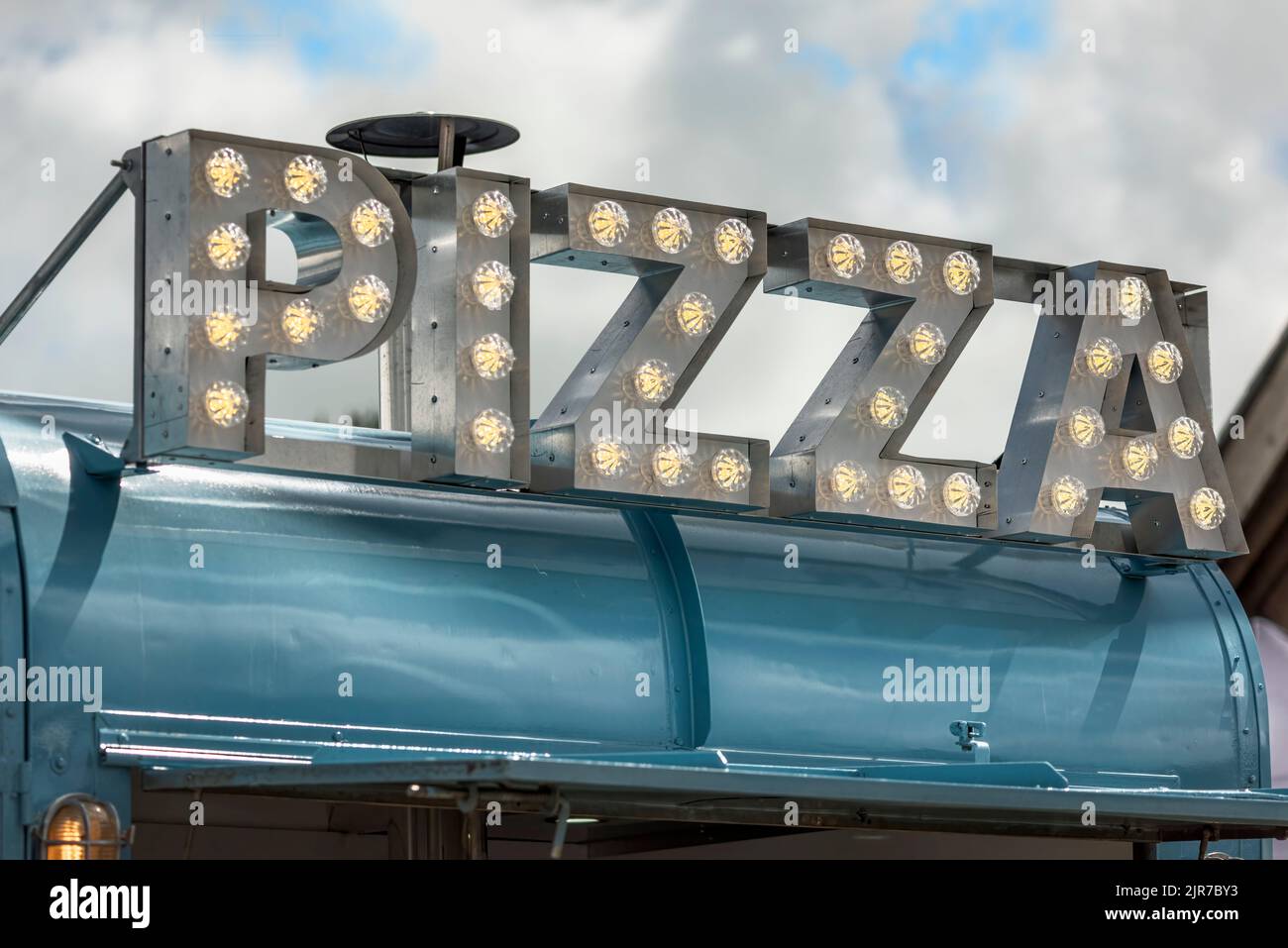 An LED illuminated Pizza sign on top of an outdoor food vendors stall. Stock Photo
