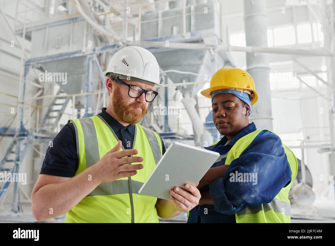 Two professional engineers with tablet scrolling through online manual guide while seeking for information about machinery usage Stock Photo