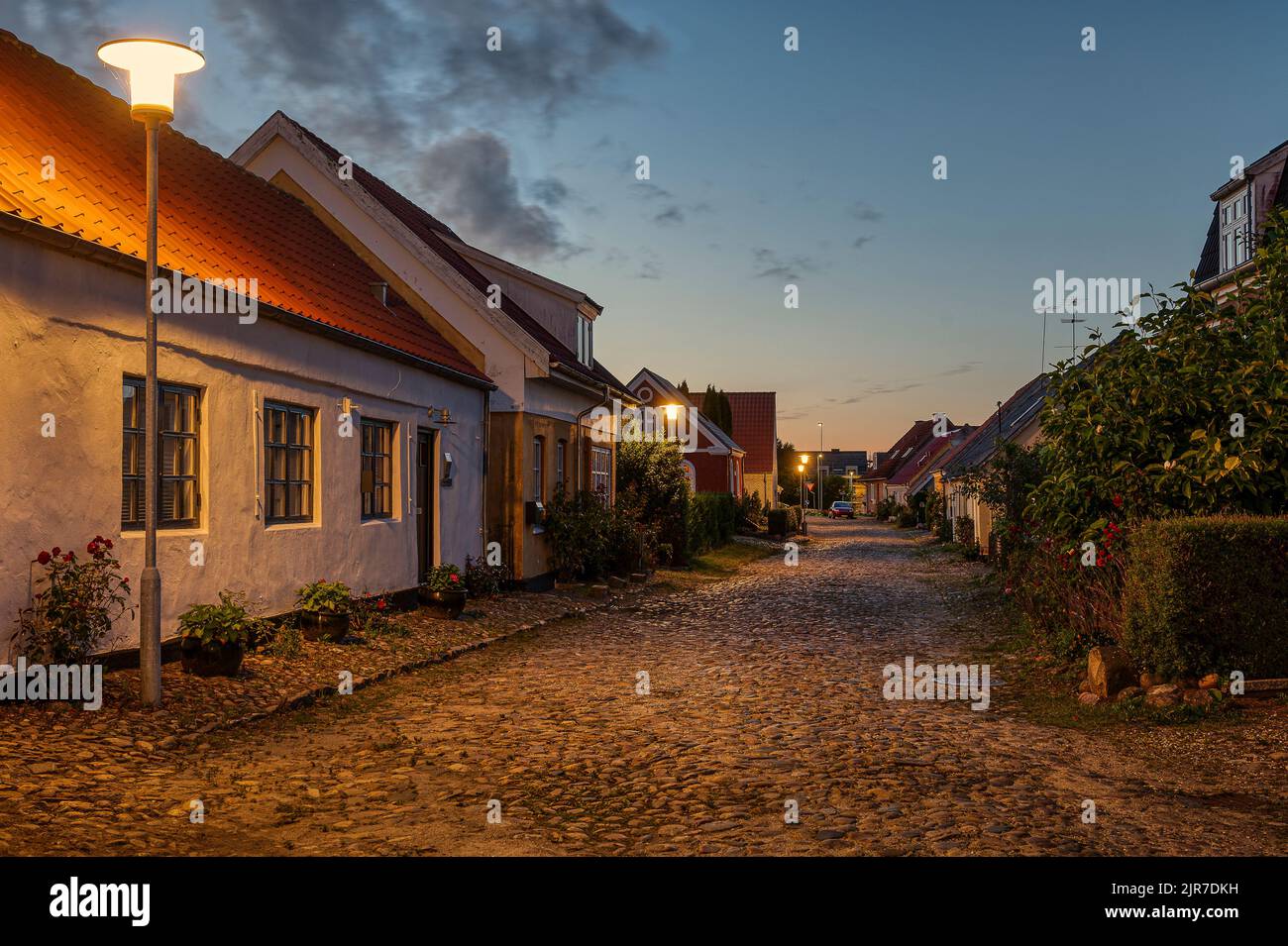 an uneven cobbled street illuminated by streetlamps and the sunset in the west, Mariager, Denmark, August 6, 2022 Stock Photo