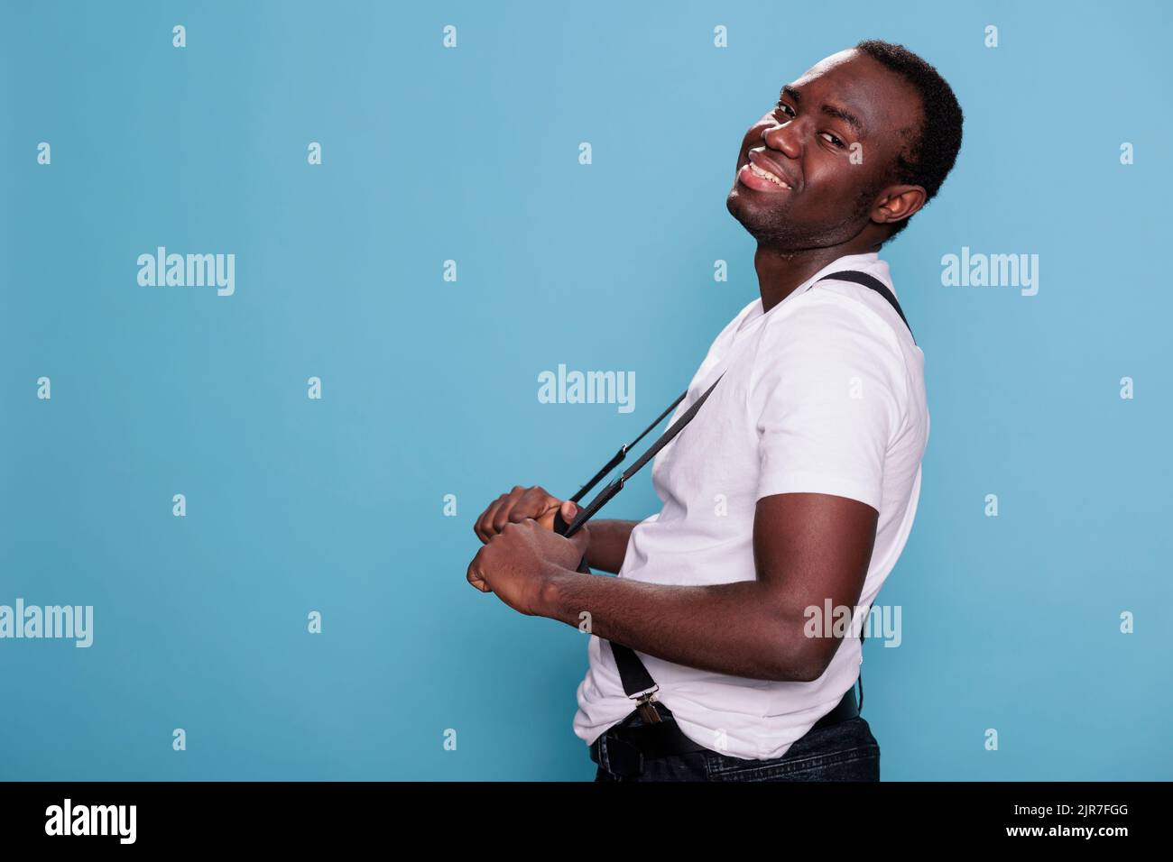 Handsome african ethnicity male model posing for camera while standing on blue background. Confident smiling heartily young man with vintage and attractive look. Studio shot Stock Photo