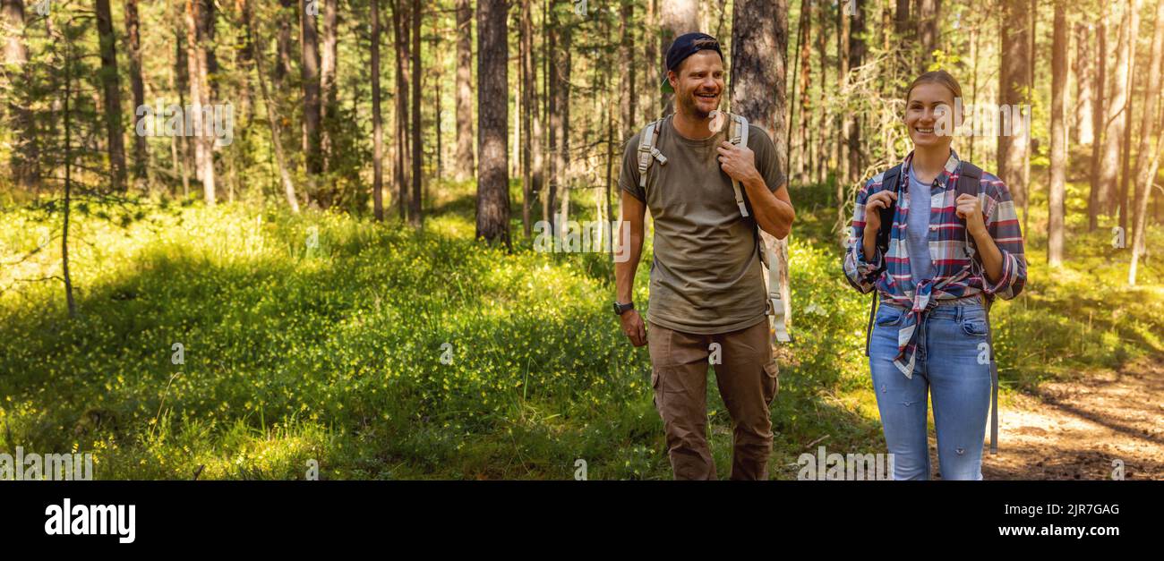 man and woman with backpacks on a forest walk on sunny summer day. outdoor adventure. banner with copy space Stock Photo