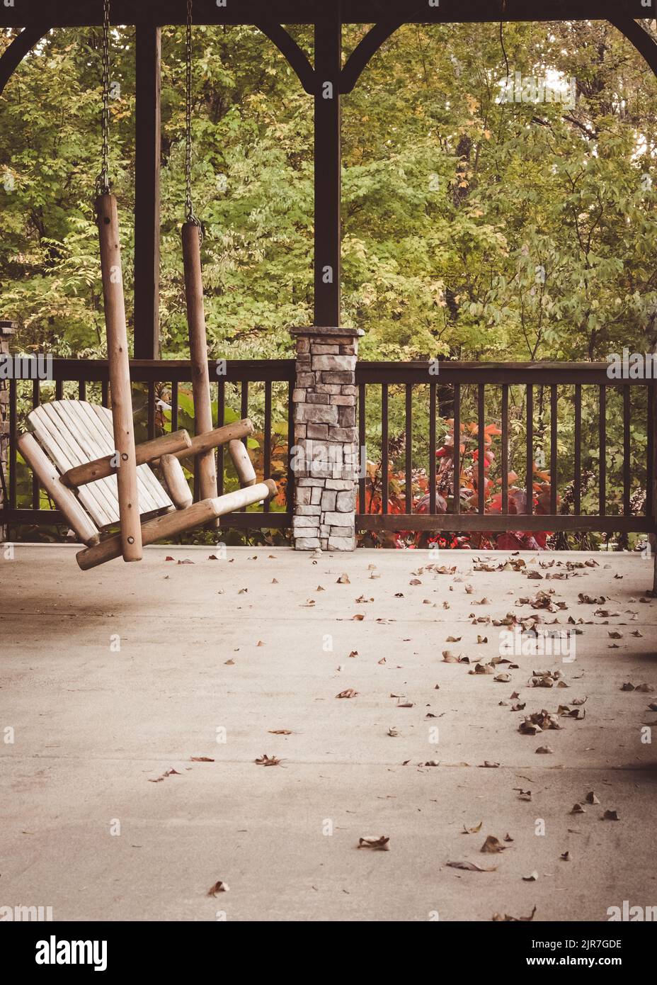 A vertical shot of a wooden swinging chair amongst autumn leaves on a veranda in Tennessee, USA Stock Photo