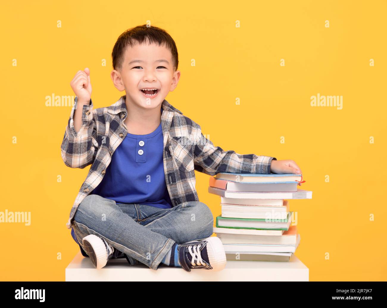Happy school boy sitting with books isolated on yellow background Stock Photo