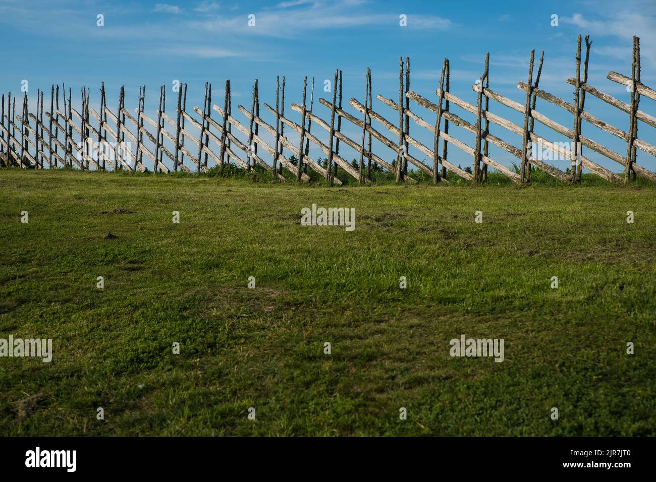 Handmade old wooden fence with green grass land and blue sky. Summer ...