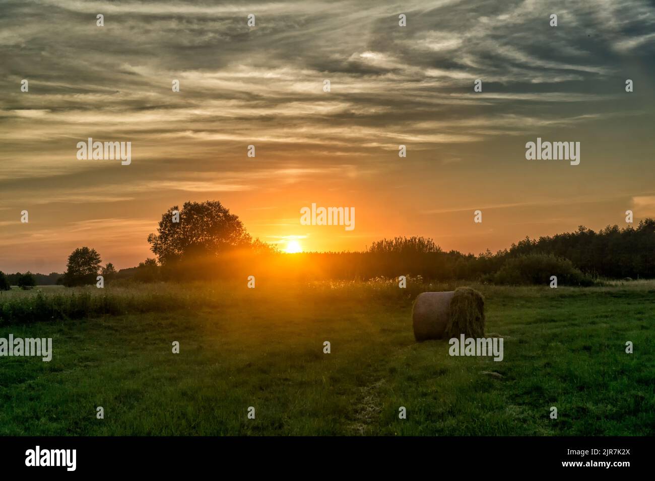 Sunset over the meadow with hay bale in summer. Landscape of Biebrza National Park in Poland, Europe. Dramatic clouds over the grassland. Stock Photo