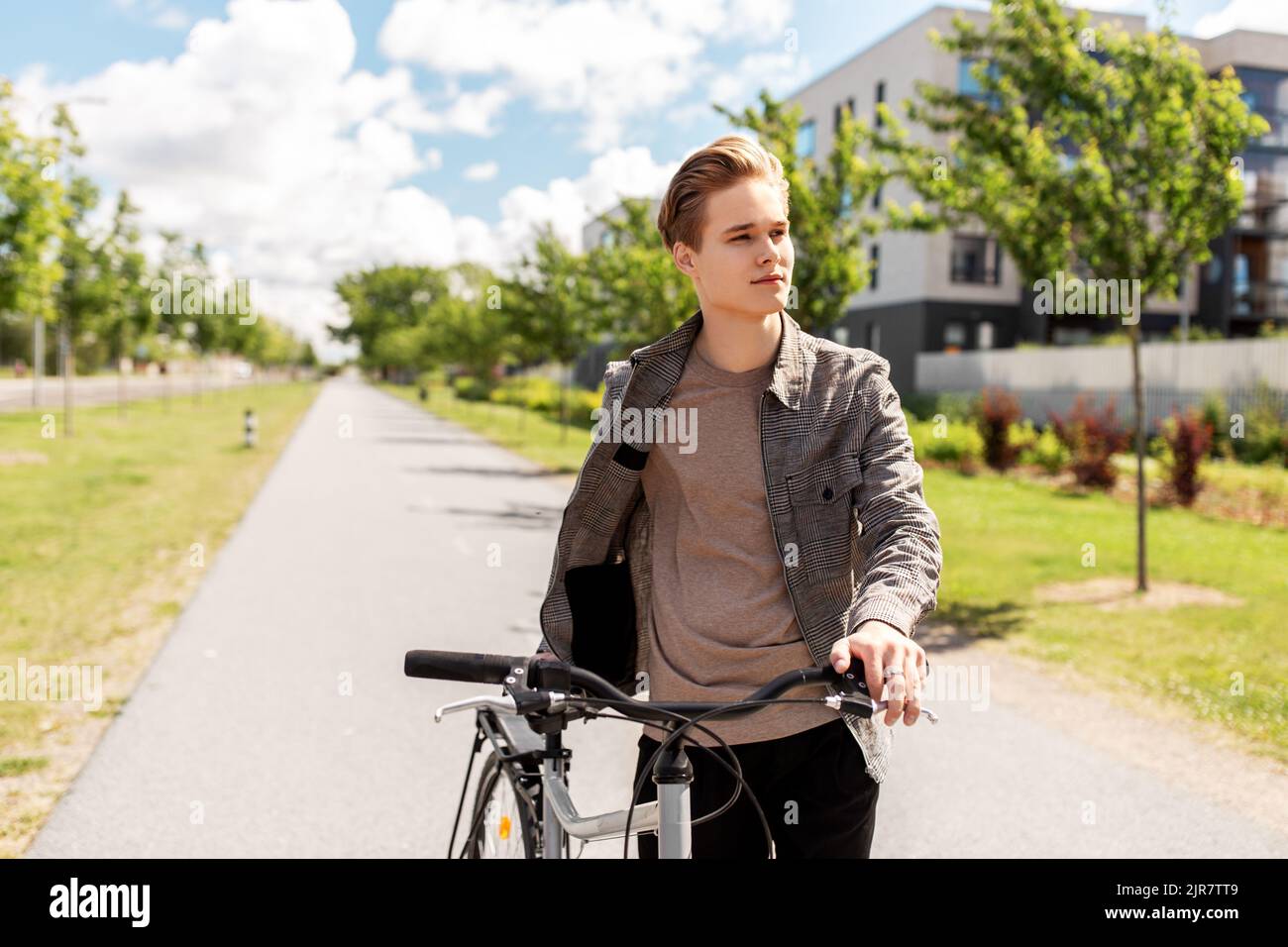 young man with bicycle walking along city street Stock Photo