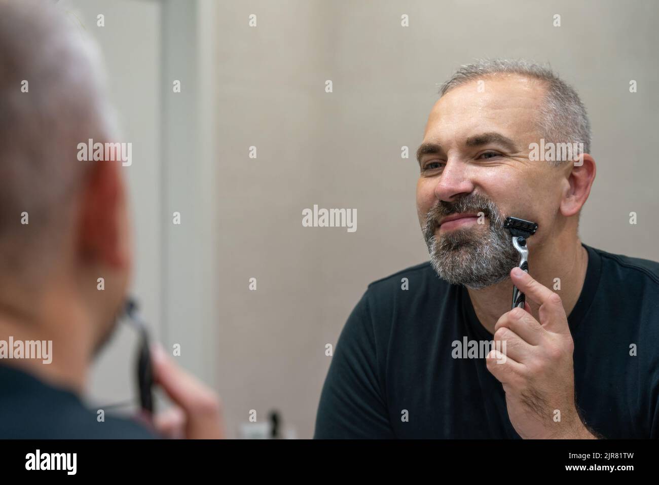 Middle-aged handsome man using razor in bathroom Stock Photo - Alamy