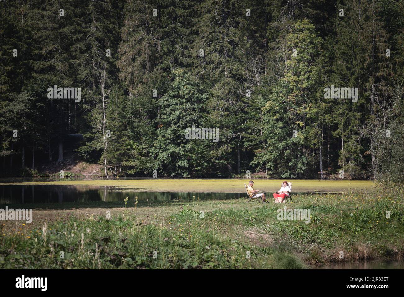 Picture of a senior couple sitting together in front of the lake zgornje jezersko being on vacation holidays, relaxed, in summer. Stock Photo