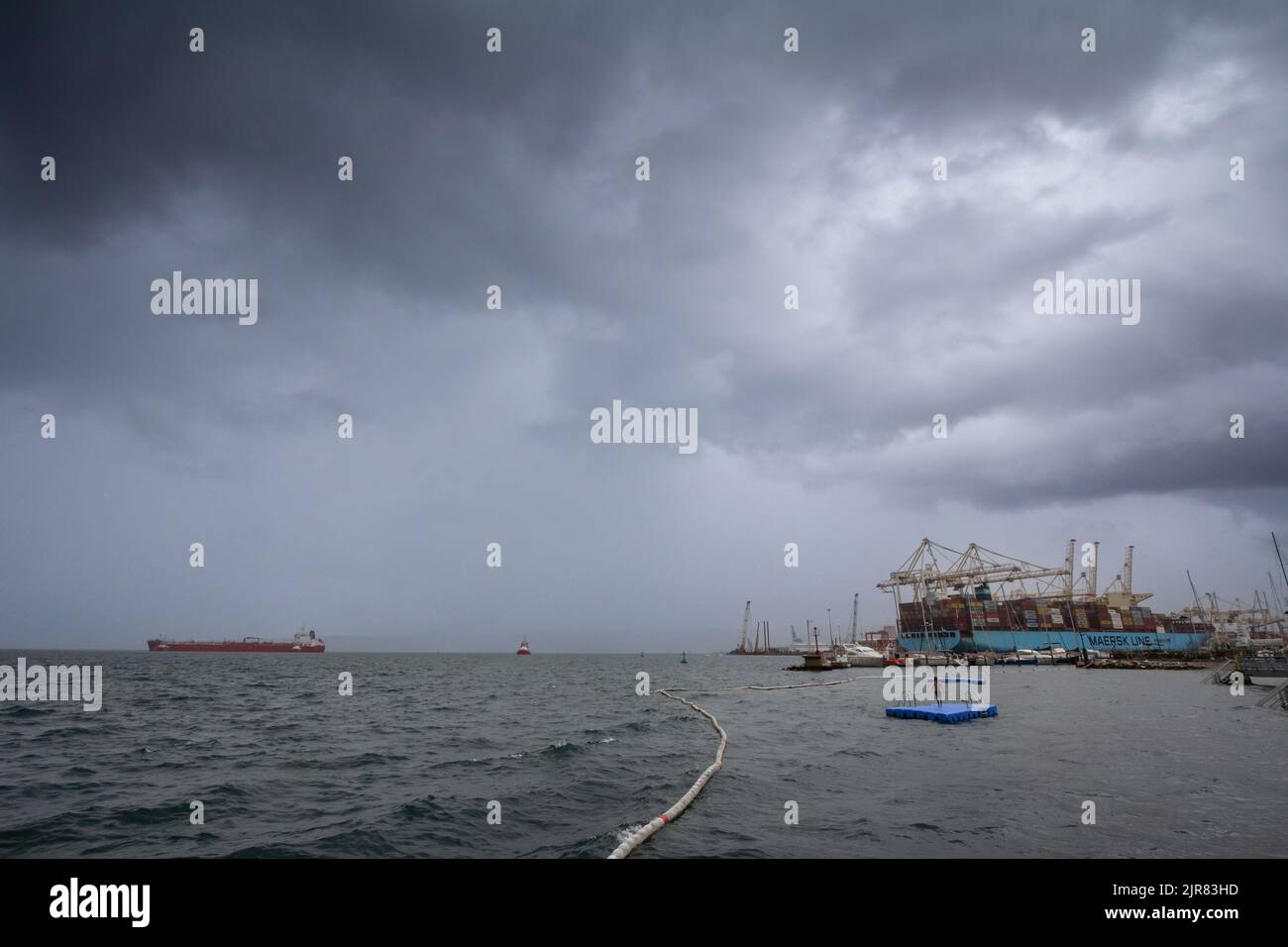 Picture of the panorama of Luka koper, the port of koper, with industrial cranes, a container ship and a kid swimming . Port of Koper is a public limi Stock Photo