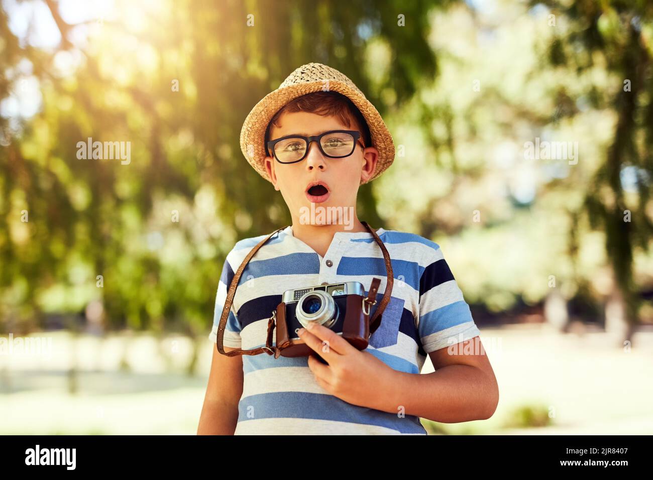 Ive got to get a picture of that. Portrait of a little boy looking surprised while taking a photo with a vintage camera at the park. Stock Photo
