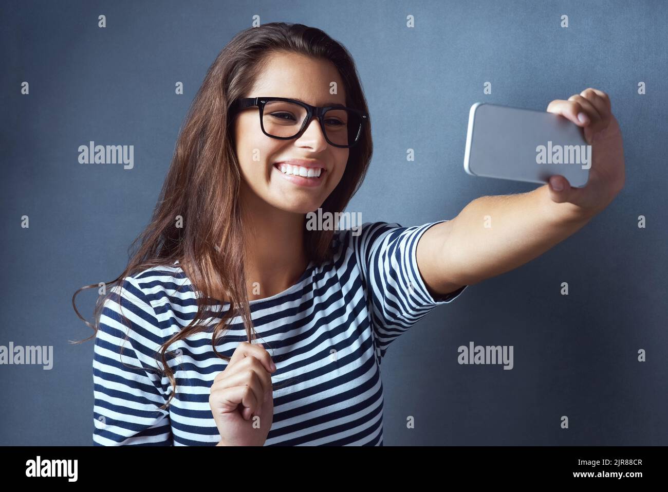 But first, lemme take a selfie. Studio shot of an attractive young woman taking a selfie against a dark background. Stock Photo