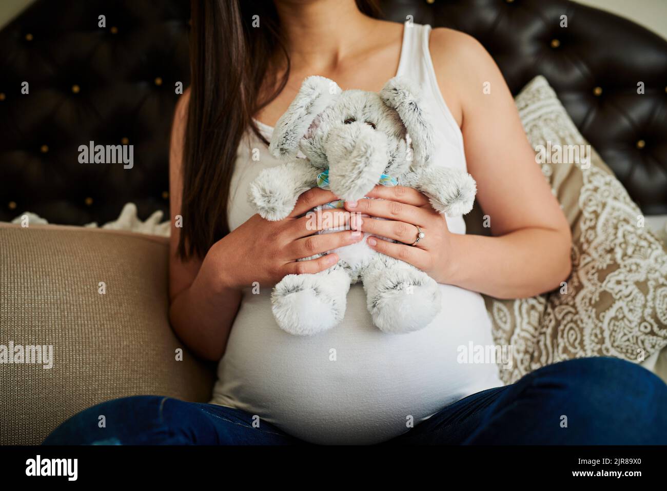 Playtime starts before her due date. an unidentifiable pregnant woman holding a stuffed toy while sitting on her bed at home. Stock Photo