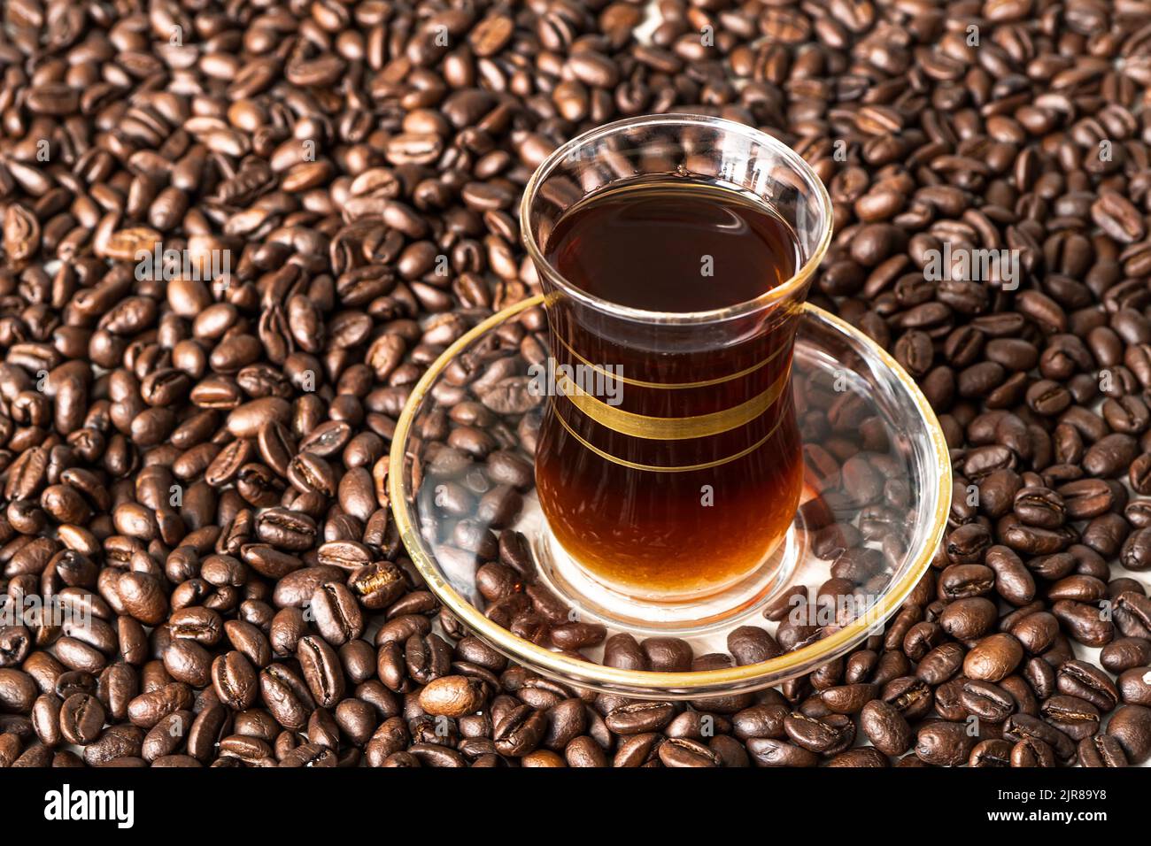 A glass mug in the traditional Turkish style with black coffee stands on coffee beans lying on