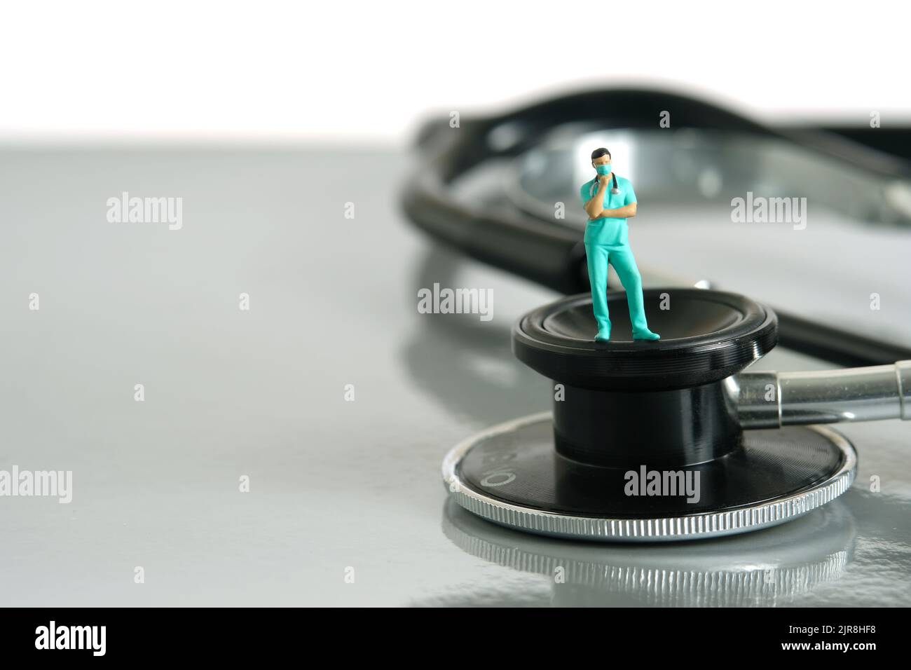 Miniature people toy figure photography. A men doctor or nurse thinking while standing above stethoscope on a desk. Image photo Stock Photo