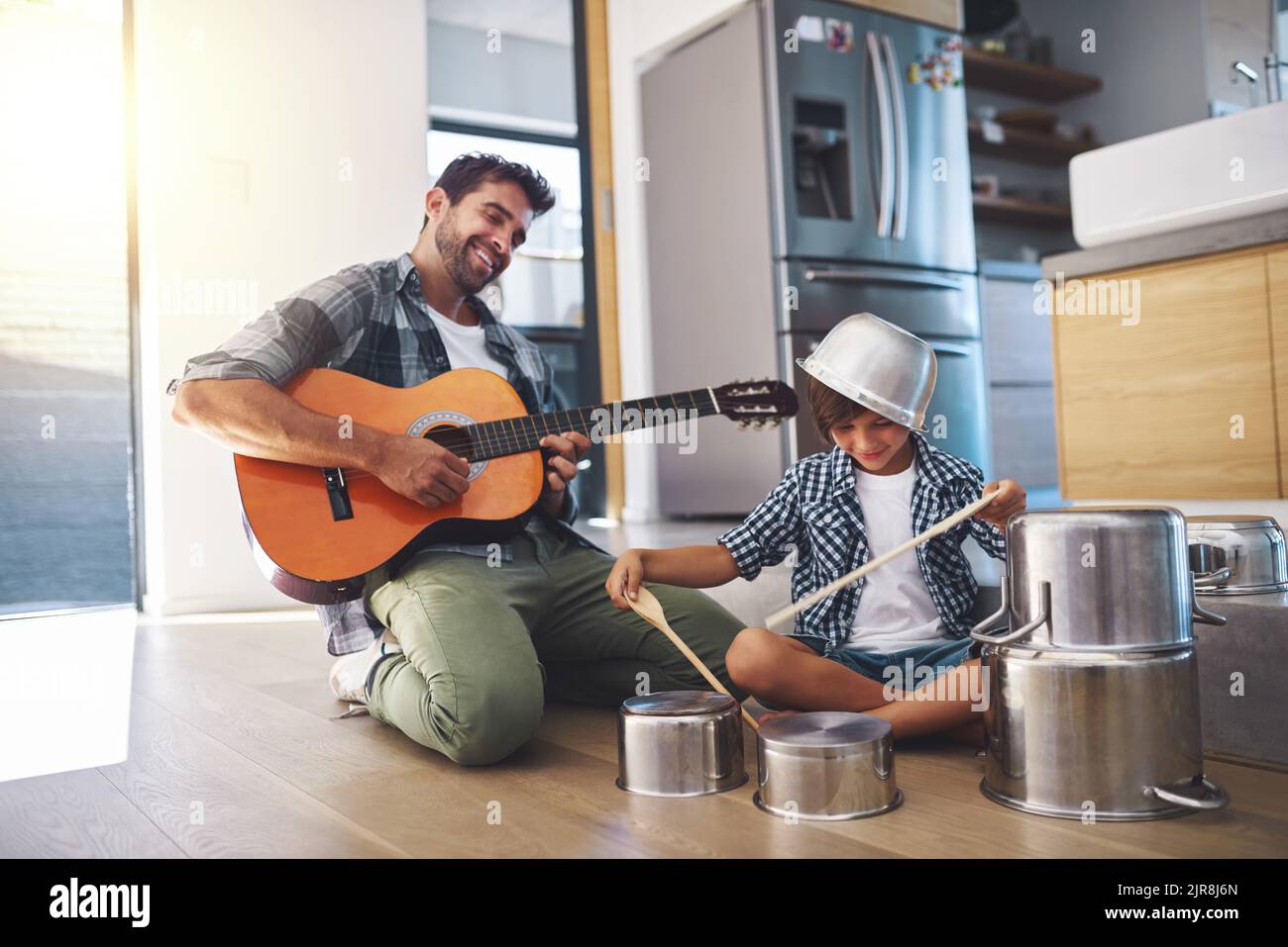 Take it away, son. a happy father accompanying his young son on the guitar while he drums on a set of cooking pots. Stock Photo