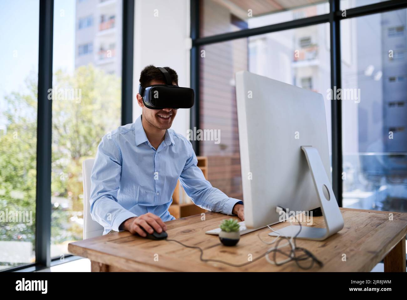 Taking his work into the virtual world. a happy young businessman wearing a virtual reality headset while working at his desk in the office. Stock Photo