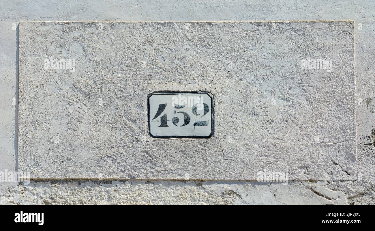 House number 452 sign fixed to old white wall. Stock Photo