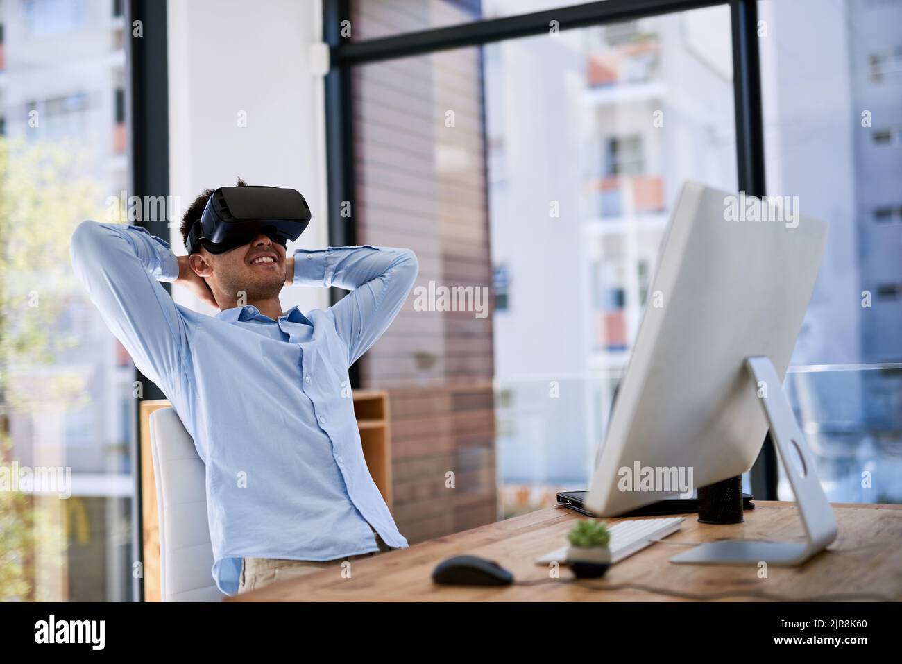 Another job well done with the help of technology. a happy young businessman wearing a virtual reality headset while working at his desk in the office Stock Photo