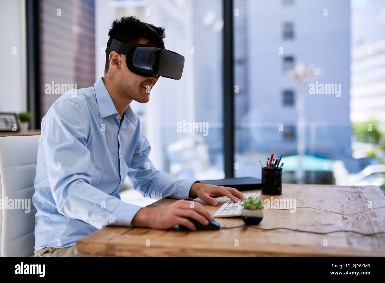 Immersed in a virtual world. a happy young businessman wearing a virtual reality headset while working at his desk in the office. Stock Photo