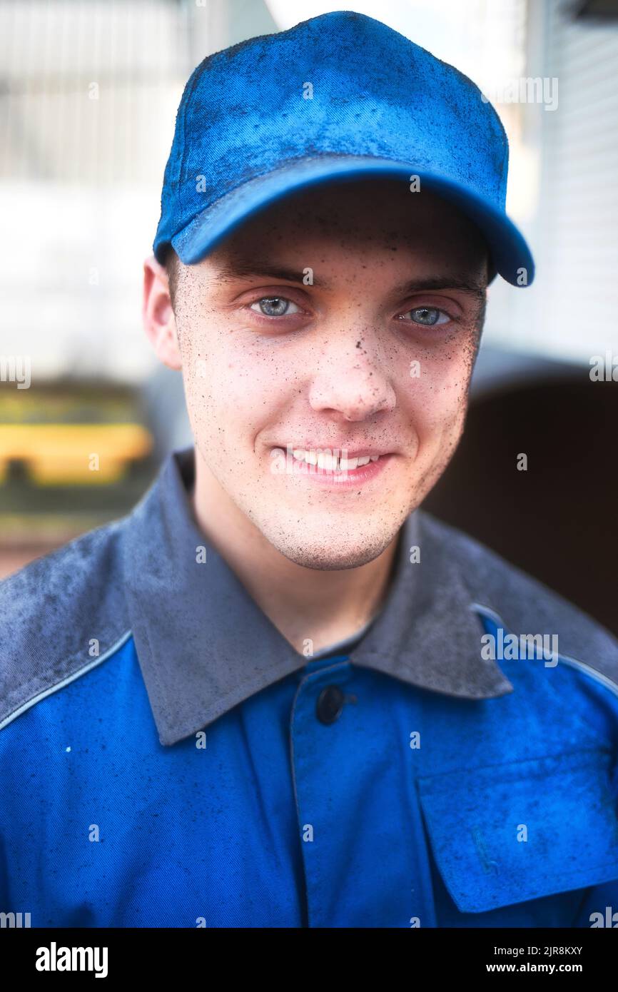 Positive emotions on face of young industrial worker in work clothes and baseball cap. Portrait of Caucasian guy. Young engineer or locksmith smiles and looks into camera. Genuine worker. Stock Photo