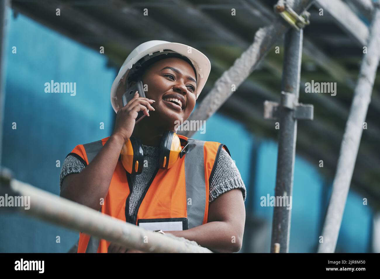 Construction manager, contractor and engineer talking on a phone while planning logistics at a building site in town. Happy, smiling and cheerful Stock Photo