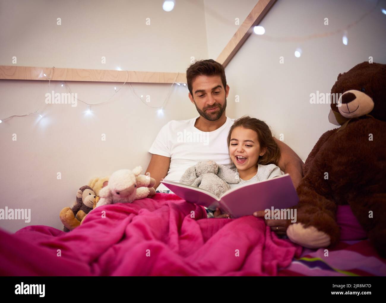 Shell be having lots of magical dreams tonight. a father reading a book with his little daughter in bed at home. Stock Photo