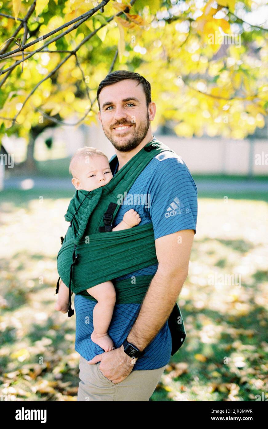 Dad with a baby in a sling standing under a tree Stock Photo Alamy